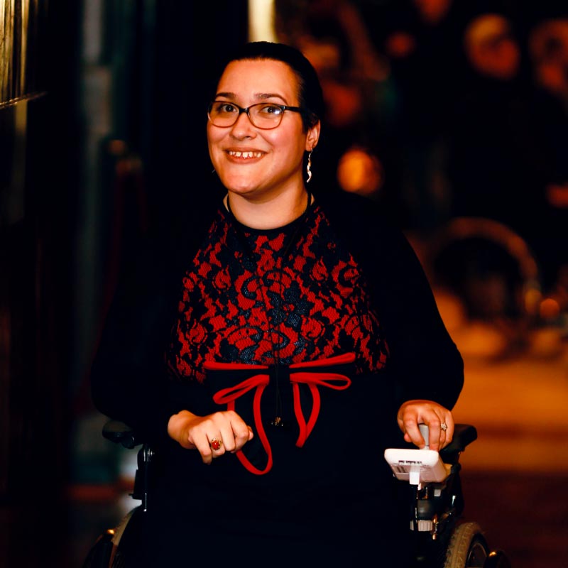 Porträt von Hiba: lächelnde Frau mit Brille und Rollstuhl