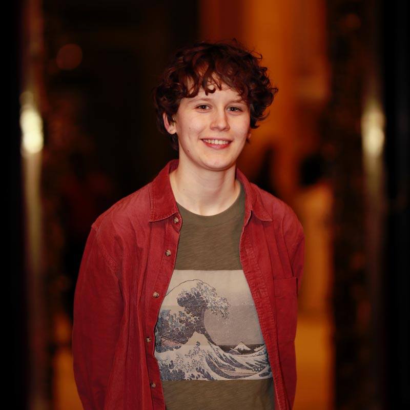 Porträt von Emilia: lächelnde, weiße Person mit kurzen, lockigen Haaren